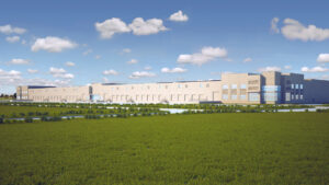 Modern industrial building amid green fields, water features, and a clear blue sky.