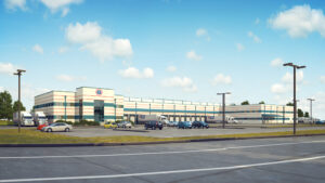 Large industrial warehouse with parking lot under clear blue sky, suburban greenery.