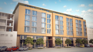 Modern multi-story building with large windows, beige-gray panels, trees, and vibrant urban surroundings.